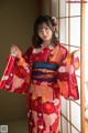 A woman in a red kimono standing in front of a window.