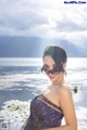 A woman in a bathing suit and sunglasses posing by the water.