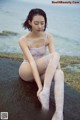 A woman sitting on a rock by the ocean.