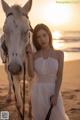 A woman in a white dress standing next to a white horse.