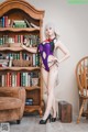 A woman in a purple lingerie posing in front of a bookcase.