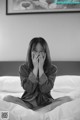 A woman sitting on a bed covering her face with her hands.