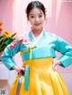 A young girl in a blue and yellow hanbok poses for a picture.