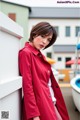 A woman in a red coat leaning against a wall.