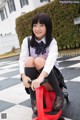 A young girl in a school uniform sitting on a red tricycle.