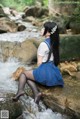 A woman sitting on a rock in a stream.