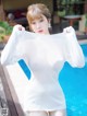 A woman in a white dress standing next to a pool.