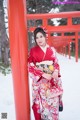 A woman in a red kimono standing in front of a red torii gate.