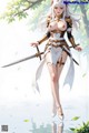 A woman in a detailed armor outfit holds a sword, standing in a serene outdoor setting with flowing leaves.