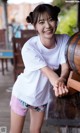 A woman in a white shirt and pink shorts leaning against a wooden barrel.