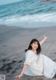 A woman in a white dress sitting on a beach.