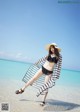 A woman in a bikini and hat standing on the beach.